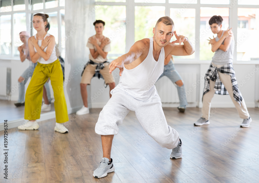 Obraz premium Young male teacher dancing hip hop dance with group of teenagers in studio