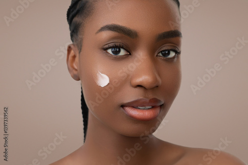 Glowing skin and a touch of cream define this beauty skincare portrait of a young African American woman with braided hair and natural makeup.