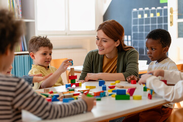 Diverse preschool children play with colorful building blocks at a classroom table, guided by a smiling teacher in a creative, inclusive early learning environment.
