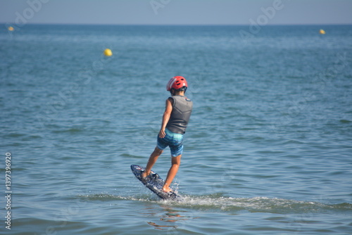 Young boy practicing hydrofoiling on the calm waters of a beach during a sunny day