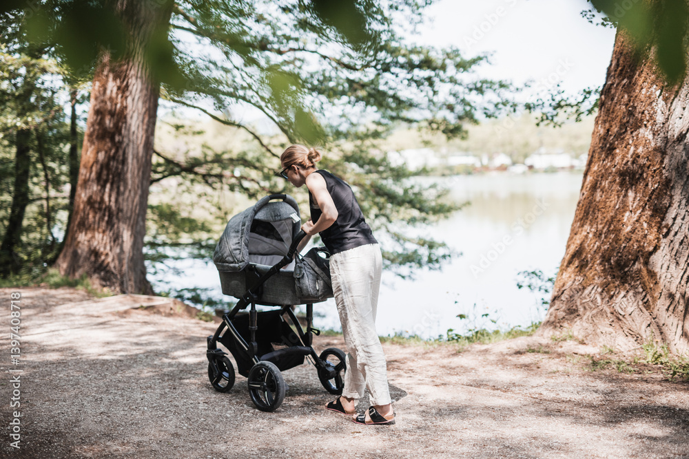 Rear view of casually dressed mother walking with baby stroller in Koseski bajer city park in Ljubljana, Slovenia. Family, child and parenthood concept. Rear view of casually dressed mother walking with baby stroller in Koseski bajer city park in Ljubljana, Slovenia. Family, child and parenthood concept.
