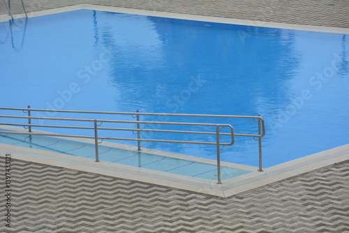 Poolside view with a smooth blue surface and metallic railing at a modern facility during daytime
