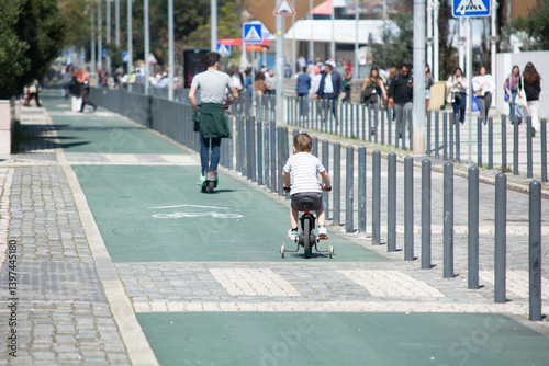 Children and adults enjoying a sunny day riding scooters and bikes on a busy urban pathway