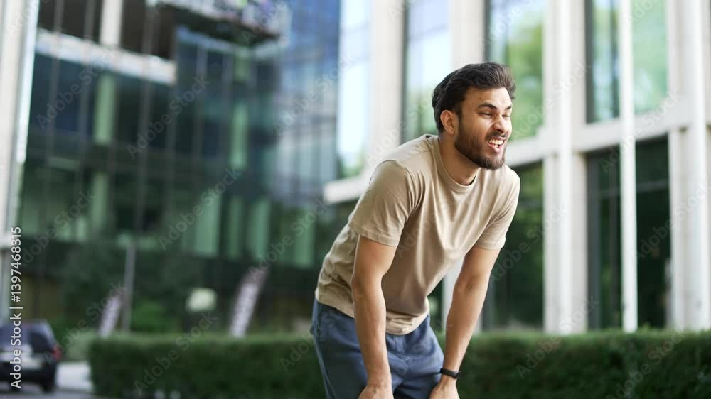 Runner has shortness of breath during a run along a city street. Athlete feels tired. Sportsman rests his hands on his knees, taking a rest break, he's breathing heavily, wipes sweat from his forehead