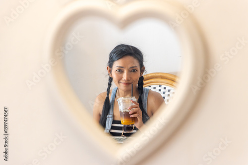 Obraz na płótnie Young woman with a drink in a plastic cup looks into a heart-shaped mirror w salonie