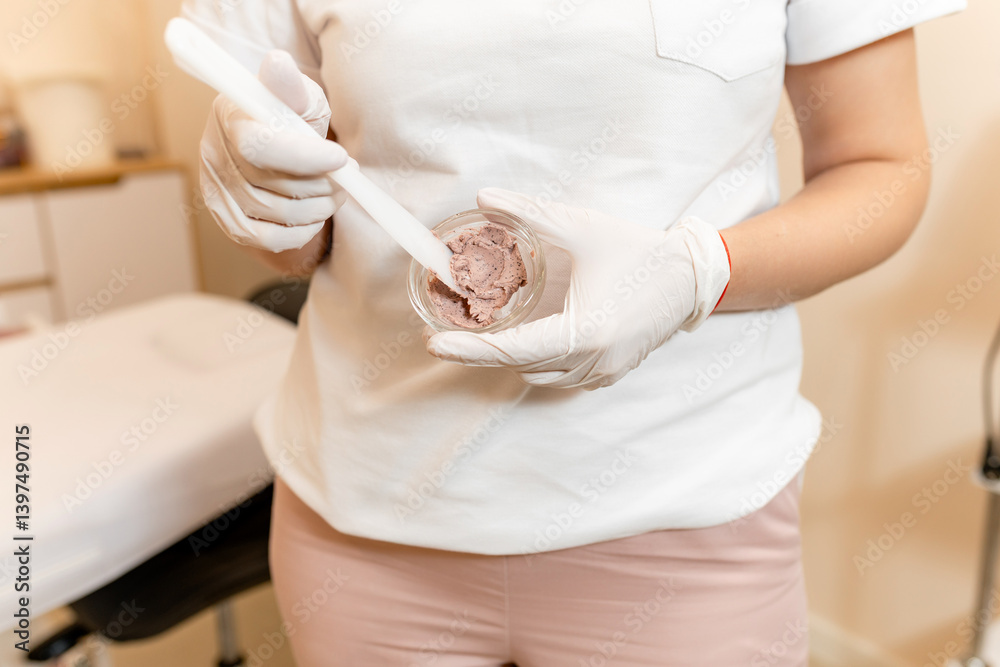 Naklejka premium In the beauty salon, the hands of the beautician mix ingredients in a small glass bowl, thereby preparing further procedures for the patient