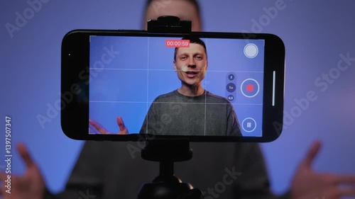 Male blogger filming video in studio or home, recording online vlog. Man using smartphone. Content creator using live broadcast on entertainment channel. Colorful RGB lighting.