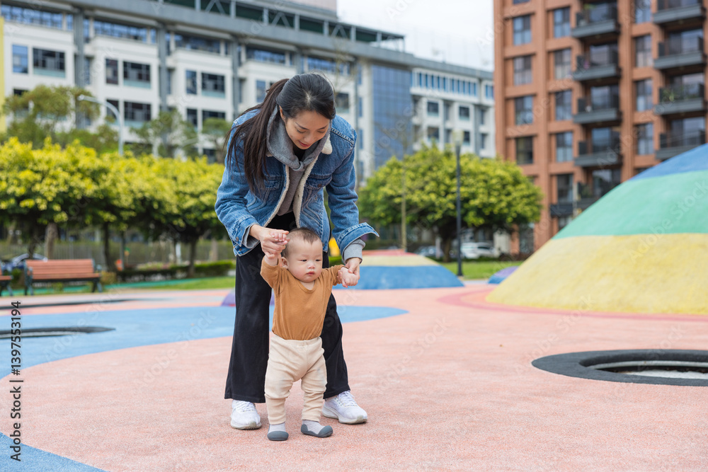 Happy mother supporting baby first steps outside