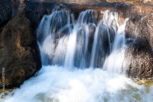 Long exposure of a small waterfall cascading over rocks with soft focus. Smooth water texture evokes a peaceful summer scene in nature. Perfect for wellness and backgrounds.
