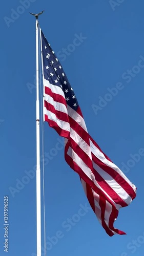 A huge American flag with stars and stripes flutters in the wind in slow motion showing the power of the USA against a blue sky on a sunny day vertical video