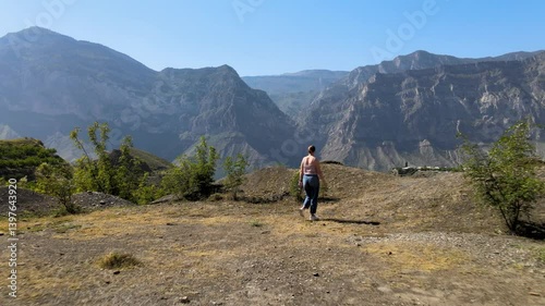 Girl strolls alone in a breathtaking mountain region. The view highlights the dramatic peaks and clear blue skies, water valley, creating a sense of tranquility and connection with nature.