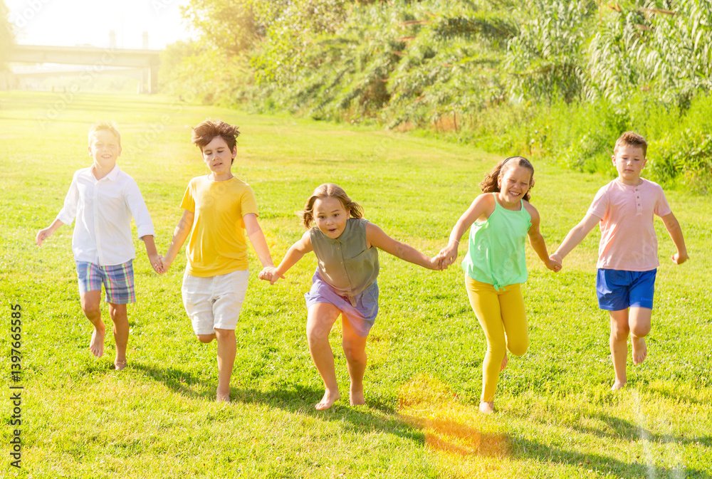 Fototapeta premium Glad young boys and girls running on green grass on field.