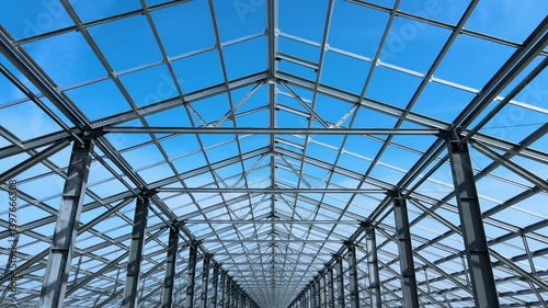 Flight inside the large metal building structure is taking shape in an agricultural zone. Metal frames are installed, creating an expansive space for future cultivation growth or animal husbandry