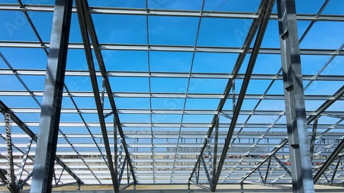 Flight inside the large metal building structure is taking shape in an agricultural zone. Metal frames are installed, creating an expansive space for future cultivation growth or animal husbandry