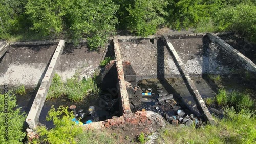 An abandoned industrial site shows waste and debris scattered amid overgrown vegetation. The polluted bitumen area highlights the impact of neglect on the environment