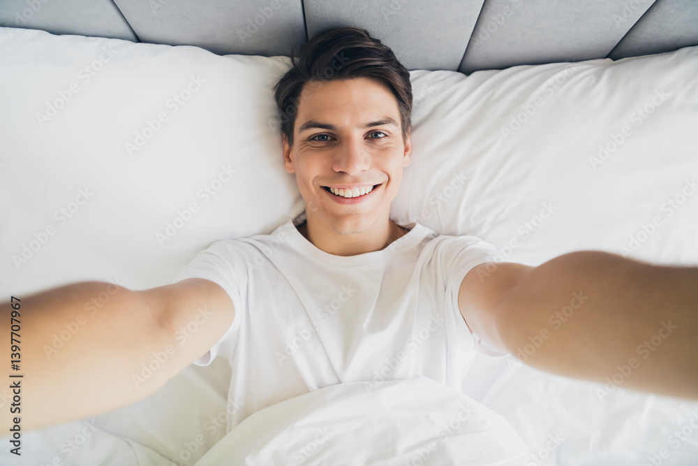 A young man waking up happily in a comfortable bed at home during a bright morning, wearing casual sleepwear and smiling cheerfully. A young man waking up happily in a comfortable bed at home during a bright morning, wearing casual sleepwear and smiling cheerfully.