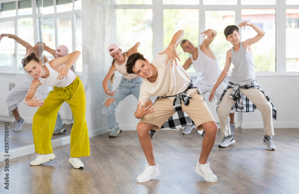 Fototapeta premium During rehearsal workout, teenage guy dances hip hop with friends against background of large mirror, window. Youth culture, active hobbies, dance subculture