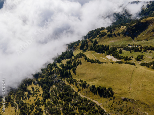 Aerial view of majestic mountains and clouds over a serene forested landscape, Stoos, Schwyz, Switzerland.