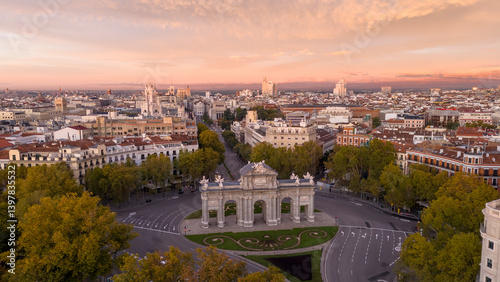 Aerial view of the beautiful Puerta de Alcala surrounded by vibrant cityscape and trees at sunset, Retiro, Madrid, Spain.