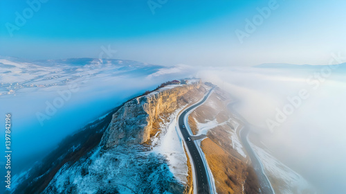Aerial view of a mountain road with fog rising and cars driving, set against a blue sky backdrop