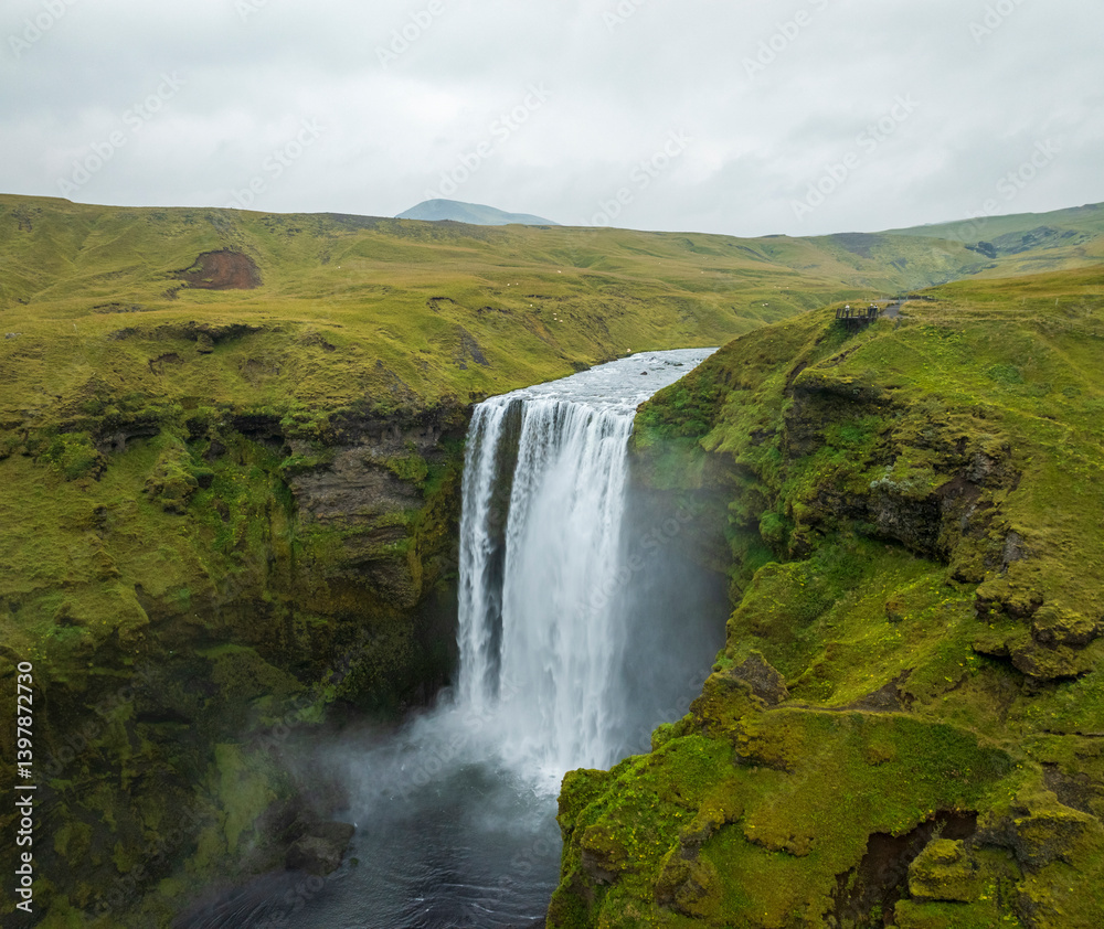 Aerial view of skogafoss waterfall cascading down a dramatic cliff surrounded by lush greenery, Hvolsvollur, Southern Region, Iceland. Aerial view of skogafoss waterfall cascading down a dramatic cliff surrounded by lush greenery, Hvolsvollur, Southern Region, Iceland.