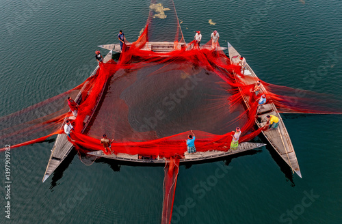 Sariakandi, Bangladesh - 17 February 2020: Aerial view of fishermen using a huge red net on tranquil water with boats, Sariakandi, Rajshahi, Bangladesh. photo