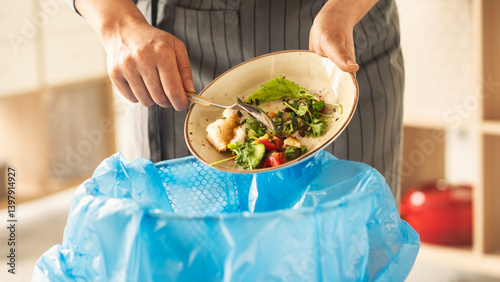 Tableau sur toile Woman scraping leftover food from plate into trash bin in kitchen