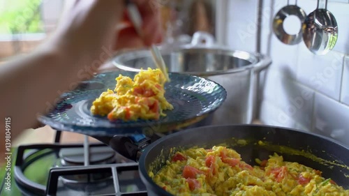 Female hands put fried eggs into glass blue plate from frying pan. Healthy hearty breakfast concept. Fried eggs for breakfast.