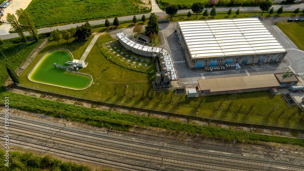 Aerial view of a warehouse near a pond and rail tracks.
