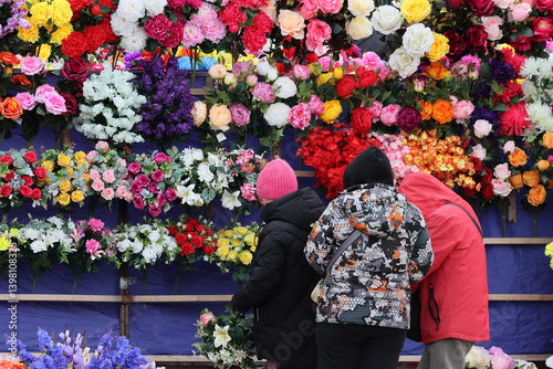 Fototapeta Naklejka Na Ścianę i Meble -  Women choose artificial ritual flowers at the market ahead of Easter