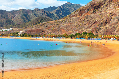 Playa de Las Teresitas in Santa Cruz from Tenerife, Canary Islands. Sandy beach curves along clear waters, bustling with people and umbrellas. Stunning coastal scene, perfect for travel photography