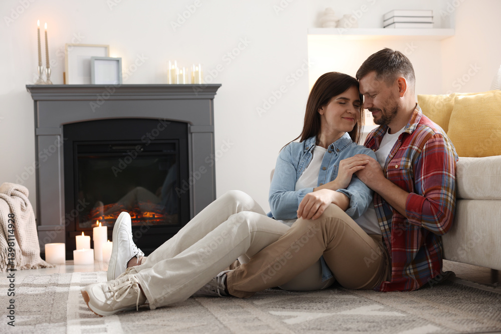 Fototapeta premium Cute couple sitting near fireplace on floor at home