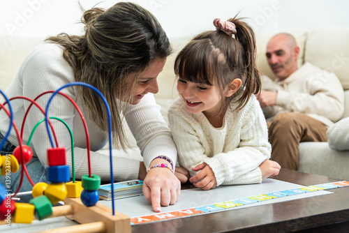 Mother teaching alphabet to her daughter at home with father watching