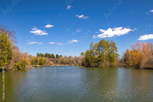 Early Spring landscape of a peaceful park lagoon beneath a blue sky and puffy white clouds in a Southeast Wisconsin, near New Berlin, Wisconsin