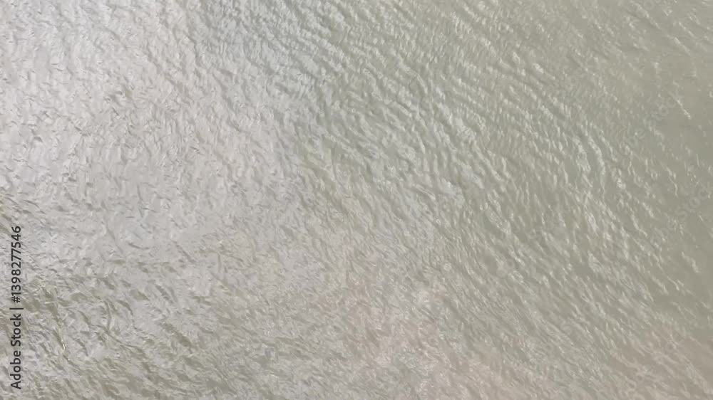 Drone image from a zenith angle of the water movement, which is a bit cloudy. The image has a slight camera movement, focusing on the water, which has slight waves. Drone image from a zenith angle of the water movement, which is a bit cloudy. The image has a slight camera movement, focusing on the water, which has slight waves.
