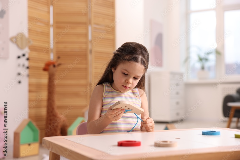 Motor skills development. Little girl playing with wooden lacing toy indoors Motor skills development. Little girl playing with wooden lacing toy indoors