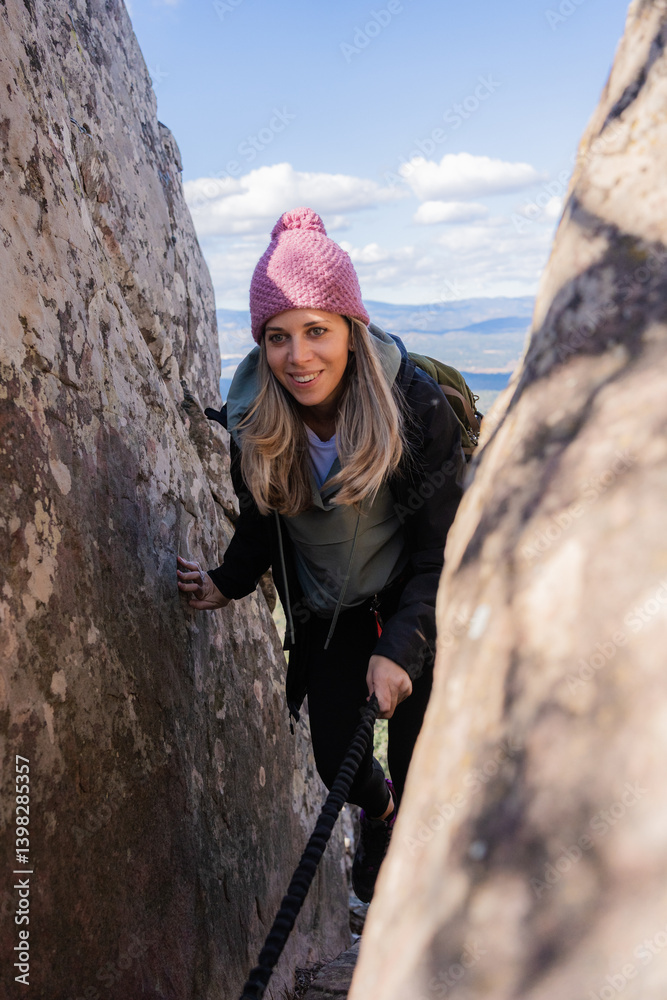 Fototapeta premium Young woman hiker descending through a narrow passage between rocks using a rope