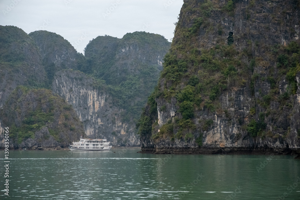 Towering limestone cliffs flank calm green waters as boats cruise between them in Ha Long Bay, Vietnam on December 27, 2019 Towering limestone cliffs flank calm green waters as boats cruise between them in Ha Long Bay, Vietnam on December 27, 2019