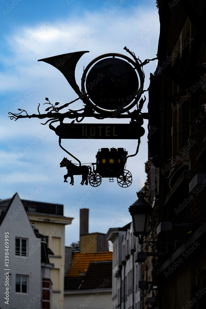 Wrought iron sign with horse carriage and french horn at dusk, in Antwerp, Belgium, silhouetted against the sky. Wrought iron sign with horse carriage and french horn at dusk, in Antwerp, Belgium, silhouetted against the sky.