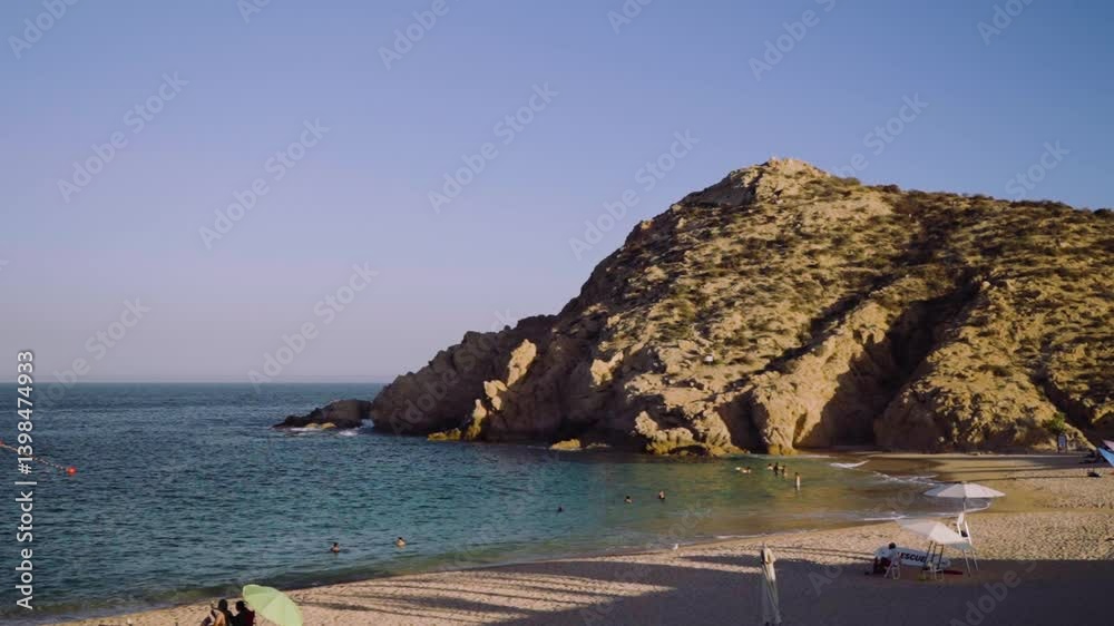 Toma de un pequeño risco en un ¡a playa mexicana, mostrando la costa, el mar llegando a la arena y personas de fondo disfrutando.
