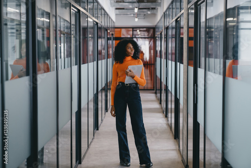 Obraz na płótnie Focused Black business executive reviewing documents on tablet while standing in corporate office. She assesses key performance indicators, aligns team goals, refines strategies for business expansion w salonie
