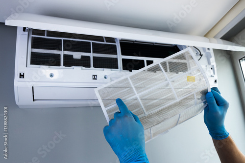A close-up view of a technician in blue gloves carefully removing an air conditioning filter from a mounted unit, emphasizing the importance of regular maintenance for optimal performance.