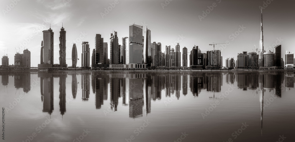 Monochrome city skyline with tall skyscrapers reflecting on calm water under a cloudy sky, Dubai Marina bay UAE