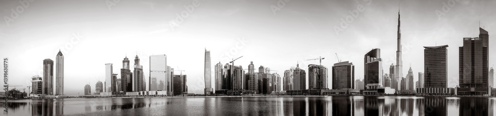Fototapeta premium Monochrome city skyline with tall skyscrapers reflecting on calm water under a cloudy sky, Dubai Marina bay UAE