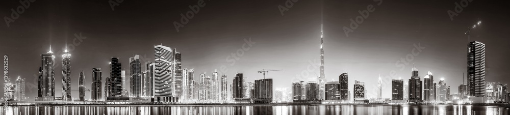 Fototapeta premium Monochrome city skyline with tall skyscrapers reflecting on calm water under a cloudy sky, Dubai Marina bay UAE