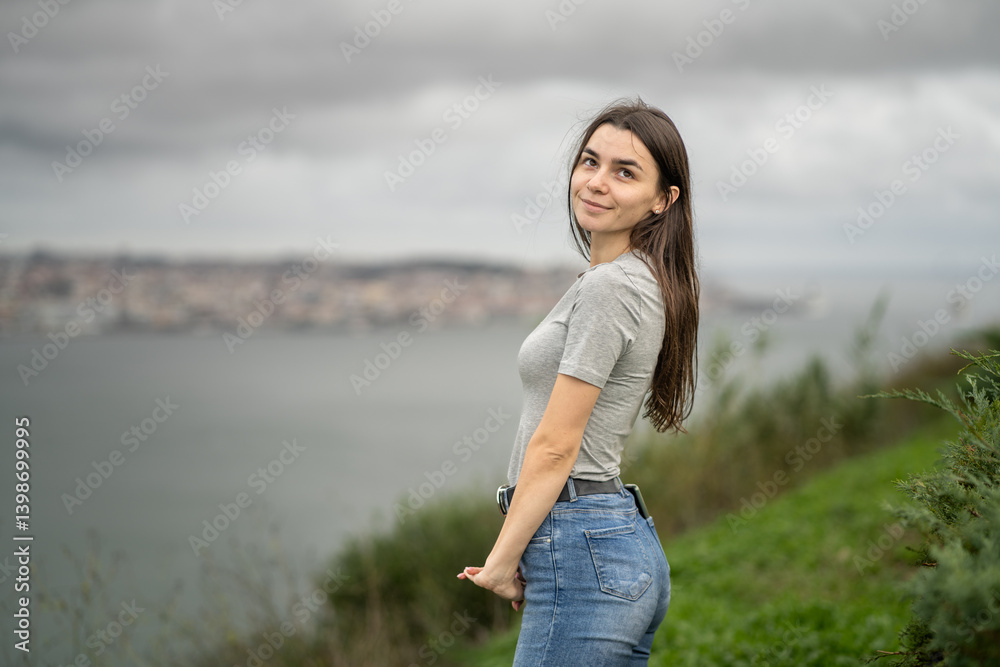 Young Woman Standing Outdoors with Scenic Ocean View and Cloudy Sky. Lisbon City in Background. Portugal Young Woman Standing Outdoors with Scenic Ocean View and Cloudy Sky. Lisbon City in Background. Portugal