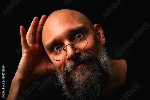 Obraz na płótnie Intense bald man with a grey beard and round glasses making a small pinch gesture. Low key portrait with dramatic lighting and expressive face on black background w salonie