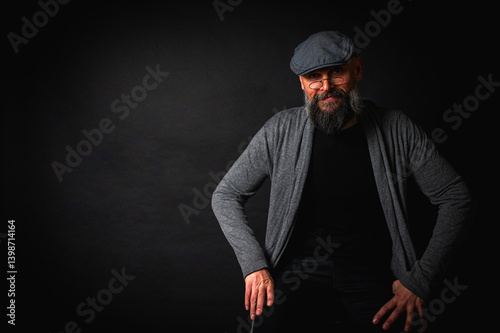 Obraz na płótnie Portrait of an emotional bearded man in a gray brass knuckles, a gray sweater and glasses looking at the camera on a dark background. Dramatic portrait in subdued lighting, expressive face, emotional w salonie