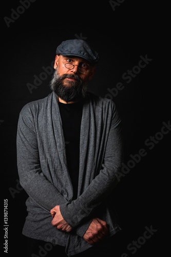 Obraz na płótnie emotional, macro portrait of a serious bearded man in a cap and glasses on a black background. Stylish, intense look with a confident and mysterious expression, emotions place for inscription on a bil w salonie
