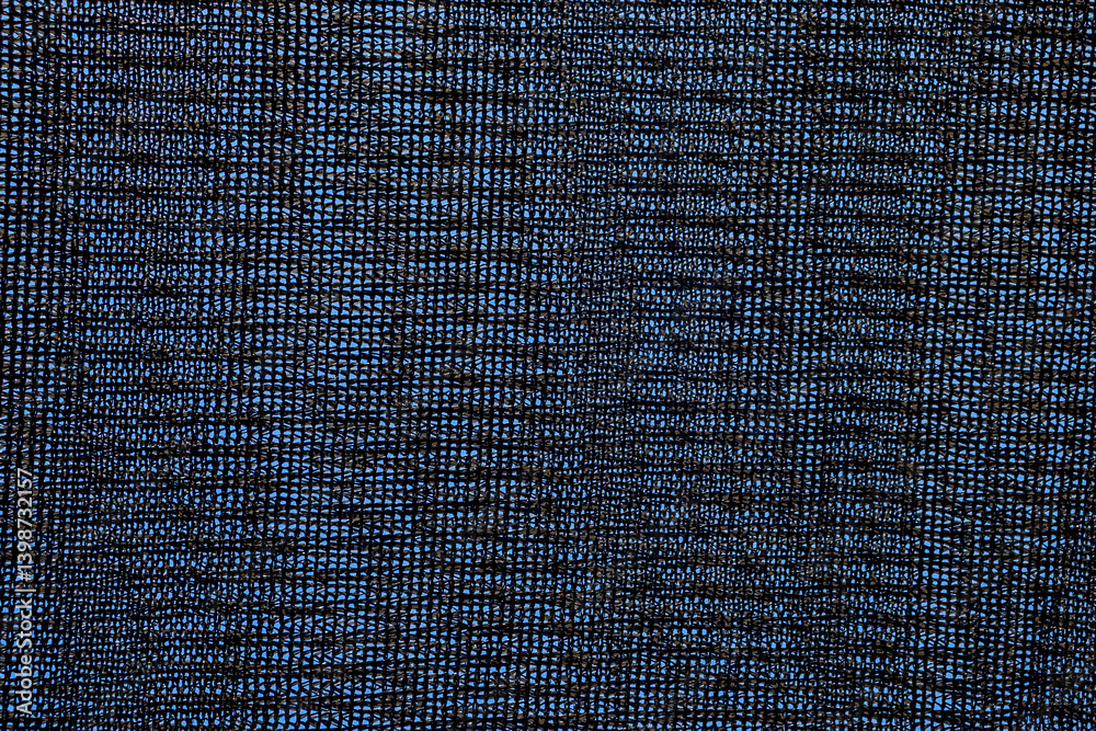 Close-up of black shading mesh against a blue sky. Commonly used in agriculture to protect crops from sunlight